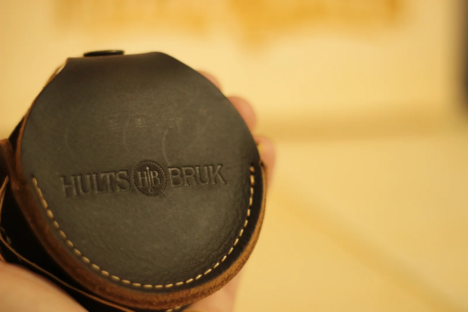 Close-up of the leather grinding stone pouch held in hand showing the HULTS HB BRUK embossed logo across the front