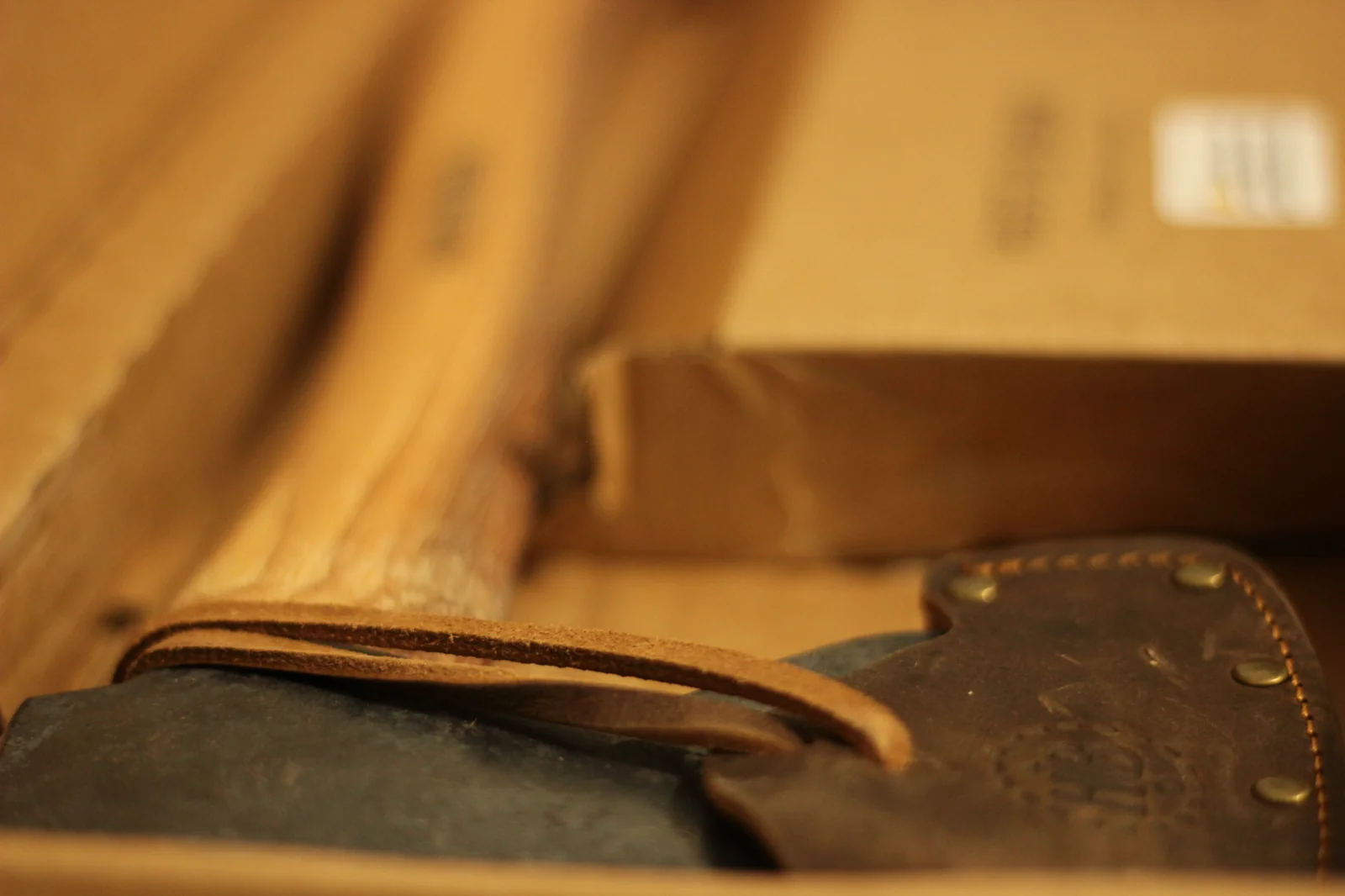 Hickory handle and leather sheath shown in the box with the leather strap of the sheath unbuttoned and hanging