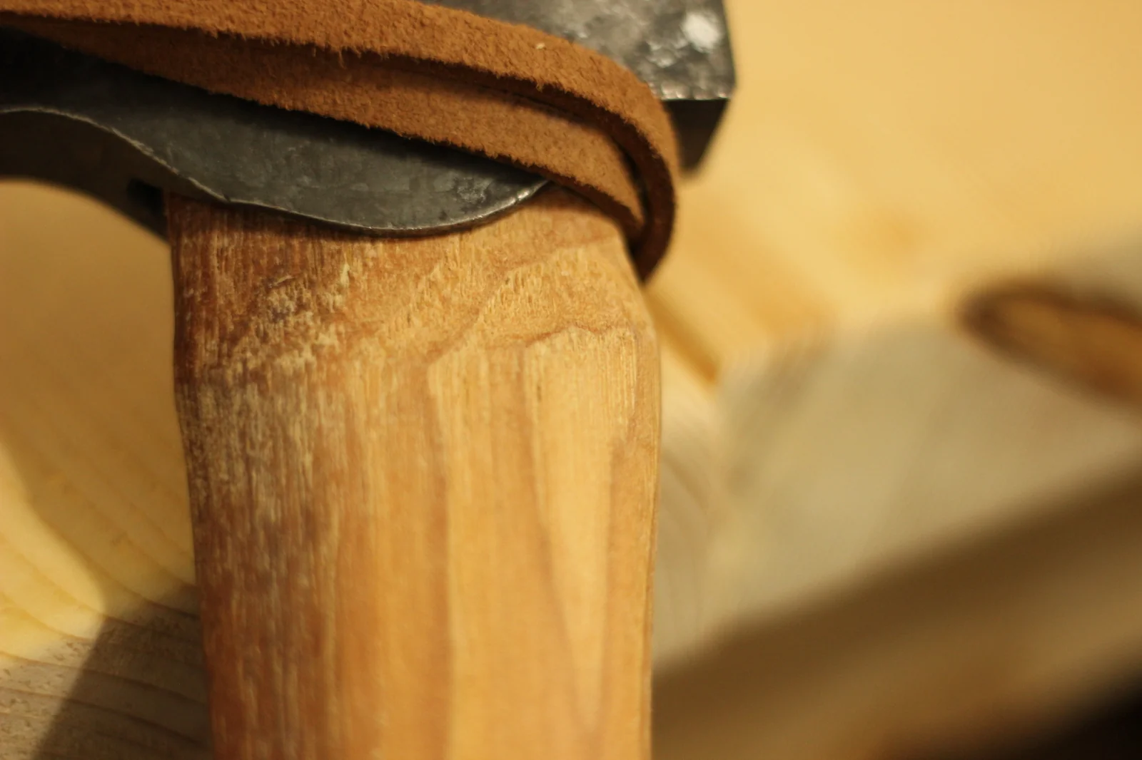 Macro shot of the join where the hickory handle meets the axe head with the leather thong looped over the head