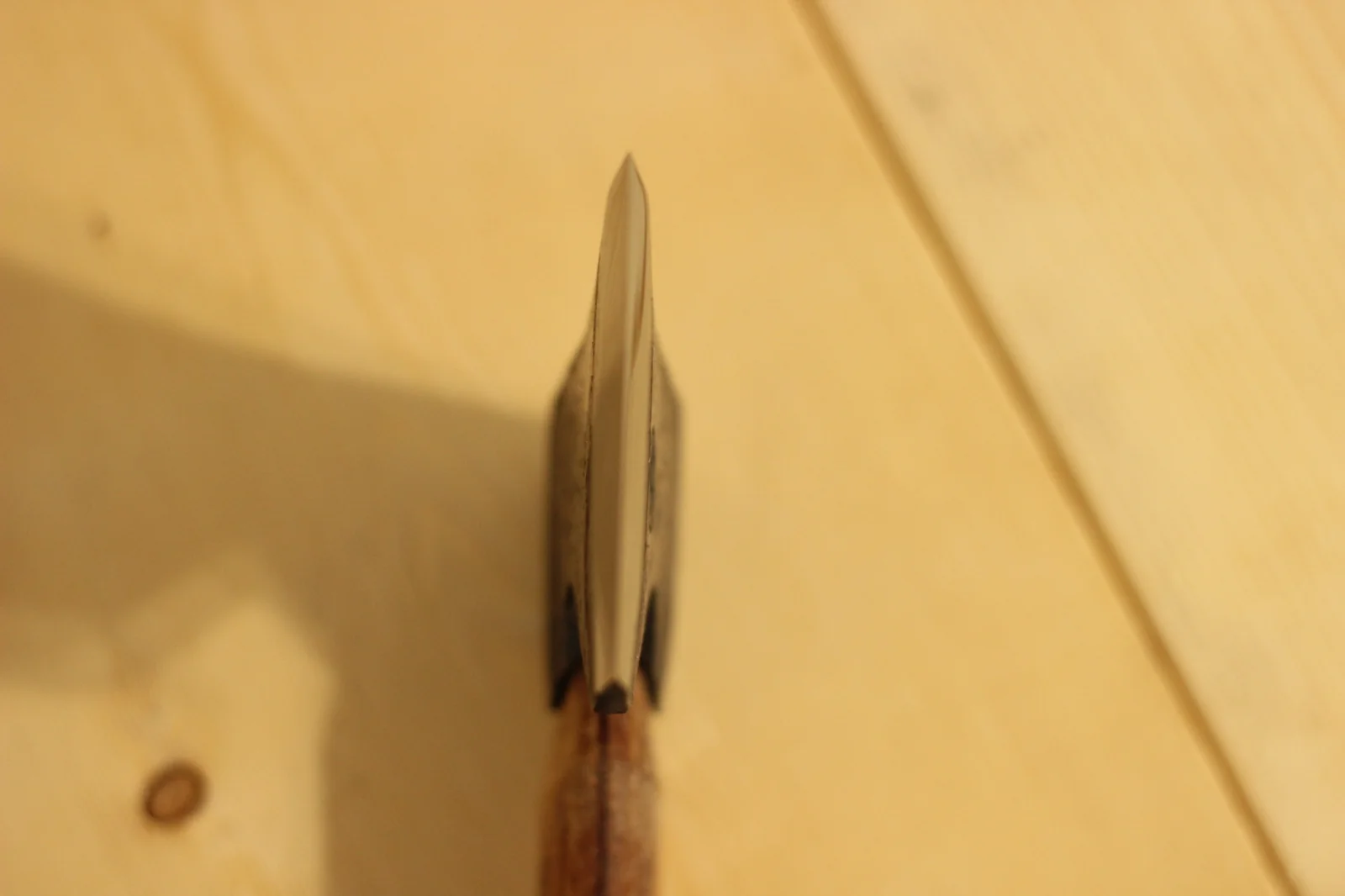 Top-down view straight along the polished cutting edge of the axe showing the symmetry of the bevel and the slight curve along the edge line