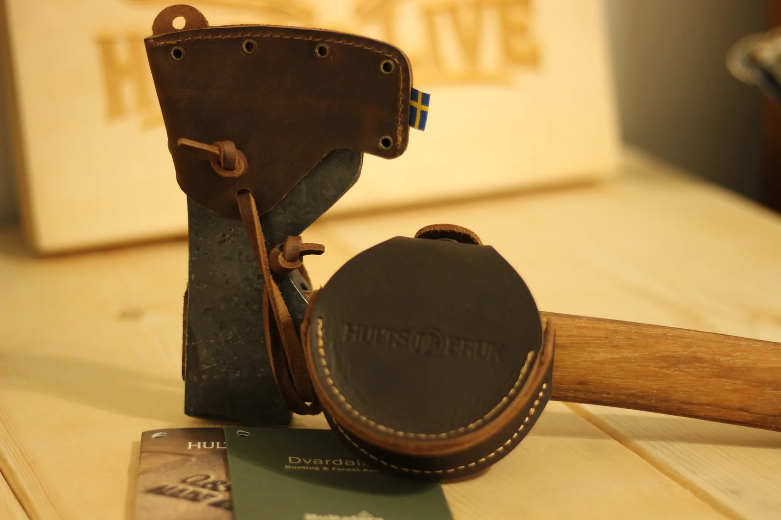 Both Hults Bruk leather pieces standing up together with the axe sheath and stone pouch visible and the Hunt and Live wooden plaque background behind