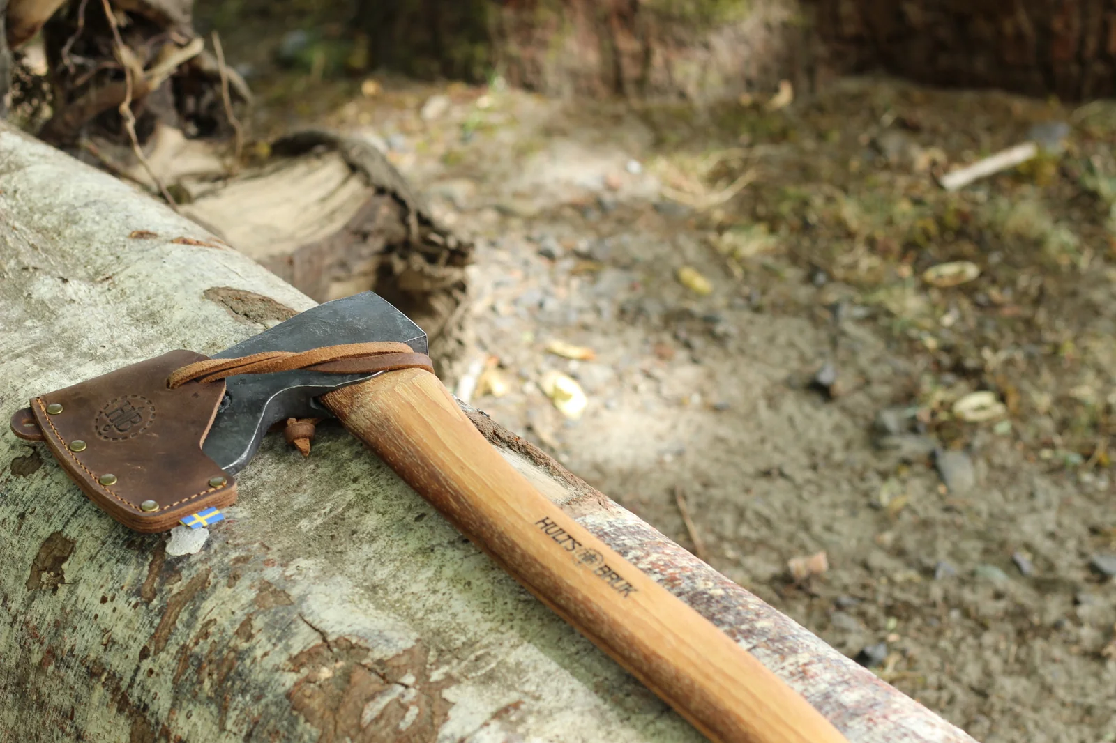 Dvärdala axe with leather sheath lying on a fallen log in an outdoor wooded setting
