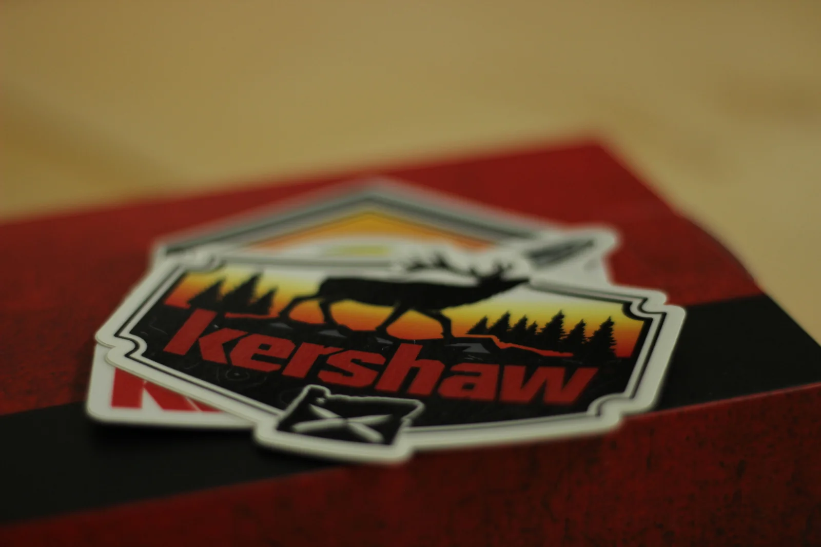 Close-up of the Kershaw deer-silhouette sticker showing a deer with antlers walking in front of a sunrise with trees in the background