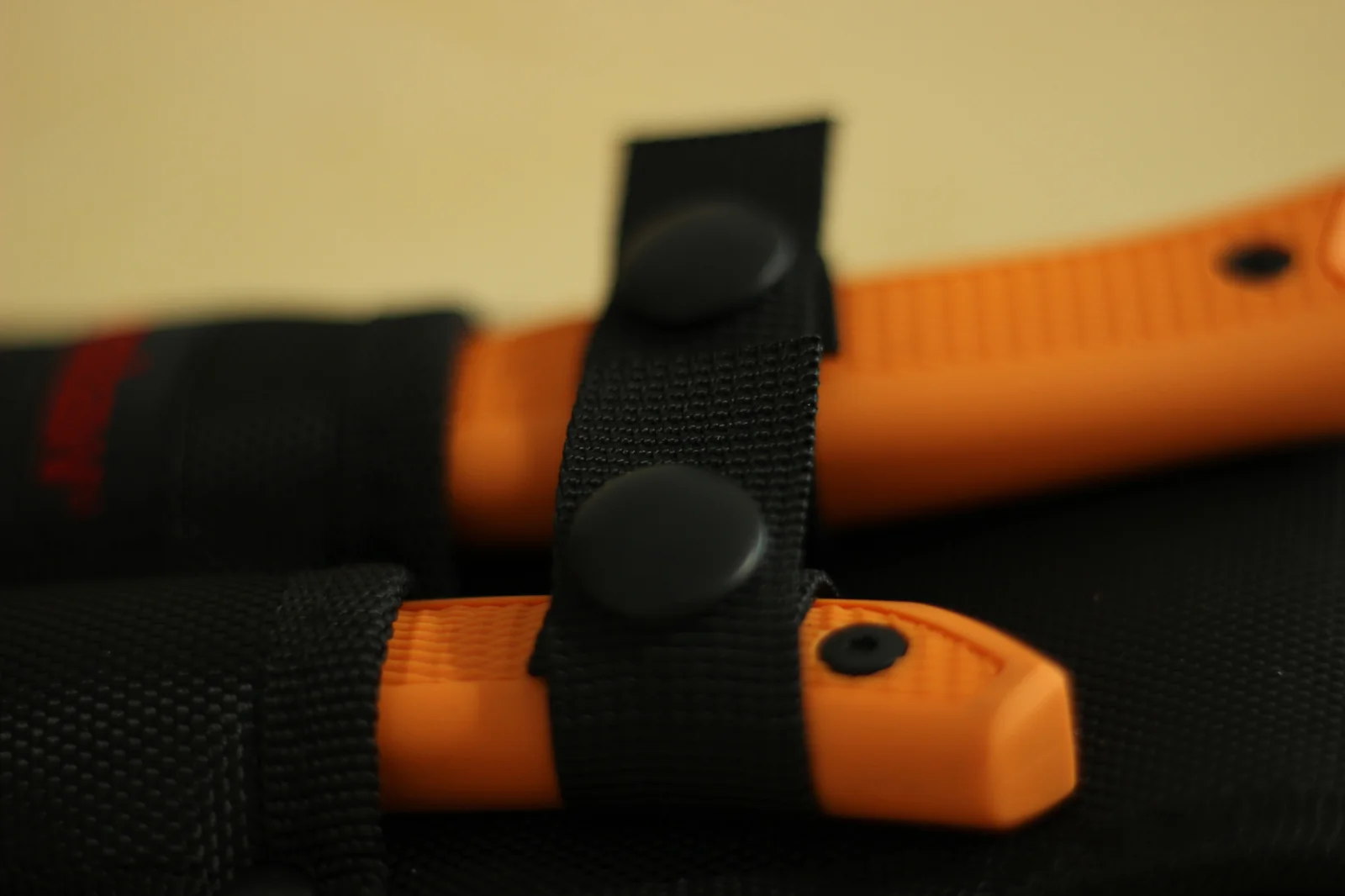 Macro of the snap closure on the retention strap showing the black plastic snap stud engaging the strap over an orange handle
