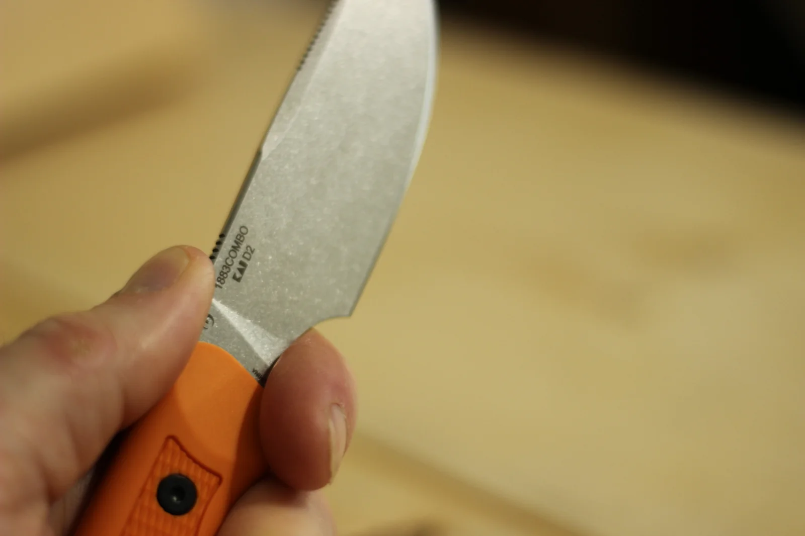 The 1883 blade held in hand showing the 1883COMBO and KAI D2 laser-etched markings on the blade with the orange handle visible at the bottom