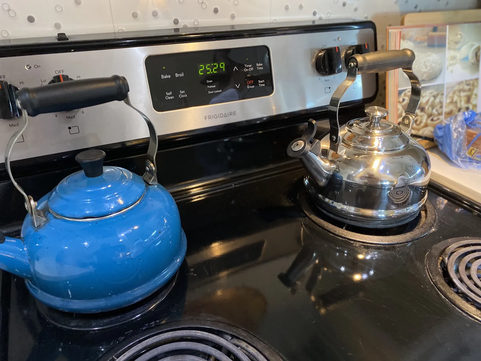 The new stainless steel Le Creuset kettle on one burner beside the older blue enamel Le Creuset kettle on another burner