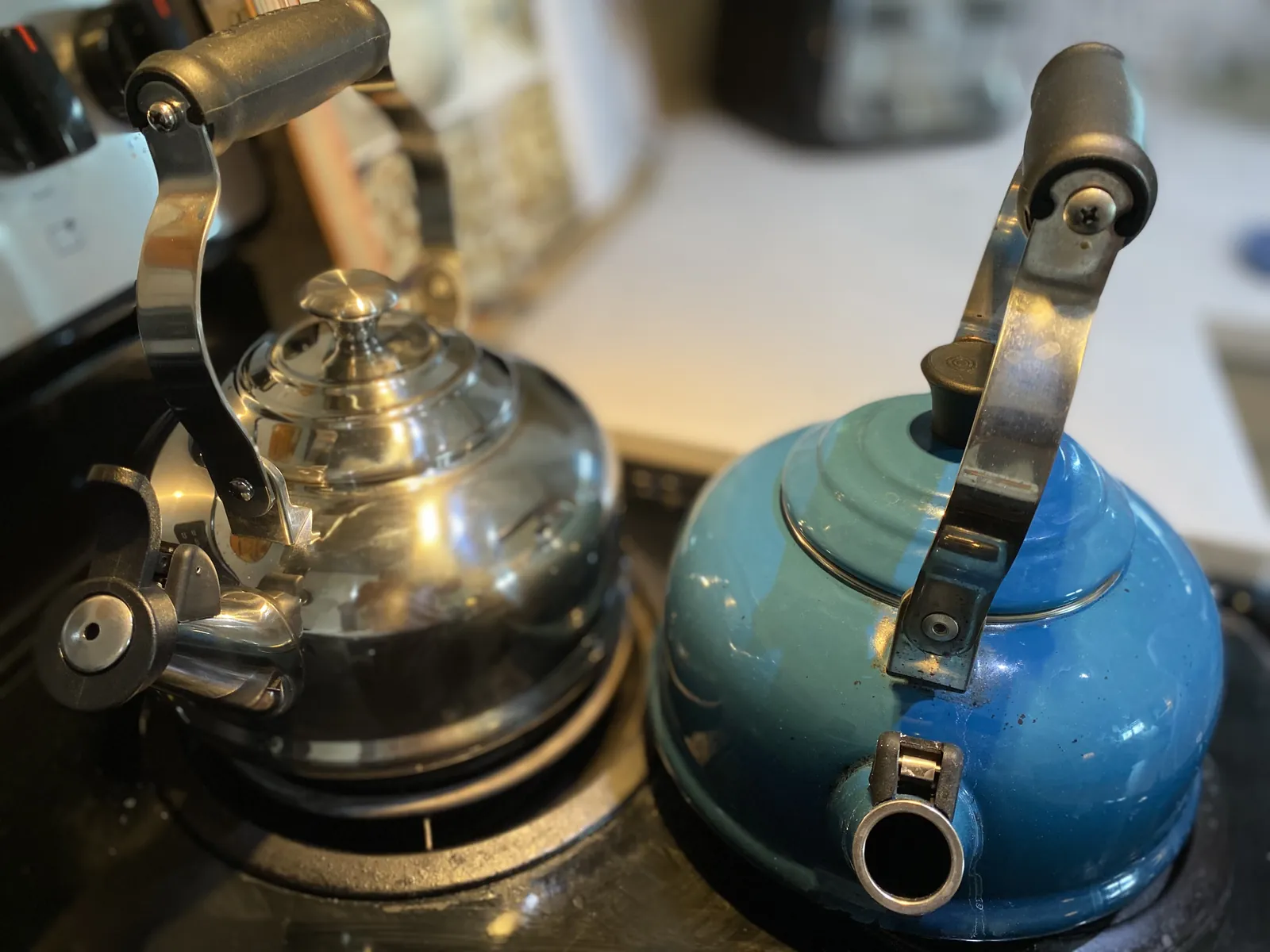 Both kettles together on the stovetop — the bare-stainless new one on the right, the worn blue enamel one on the left