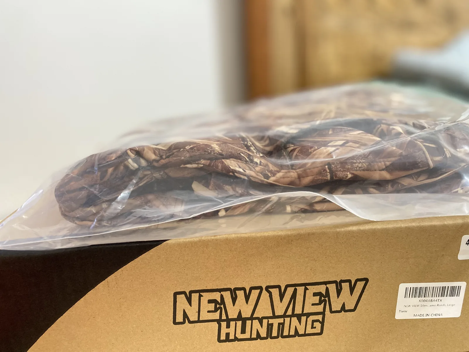 The camo jacket sealed in a clear poly bag resting on the open New View Hunting carton
