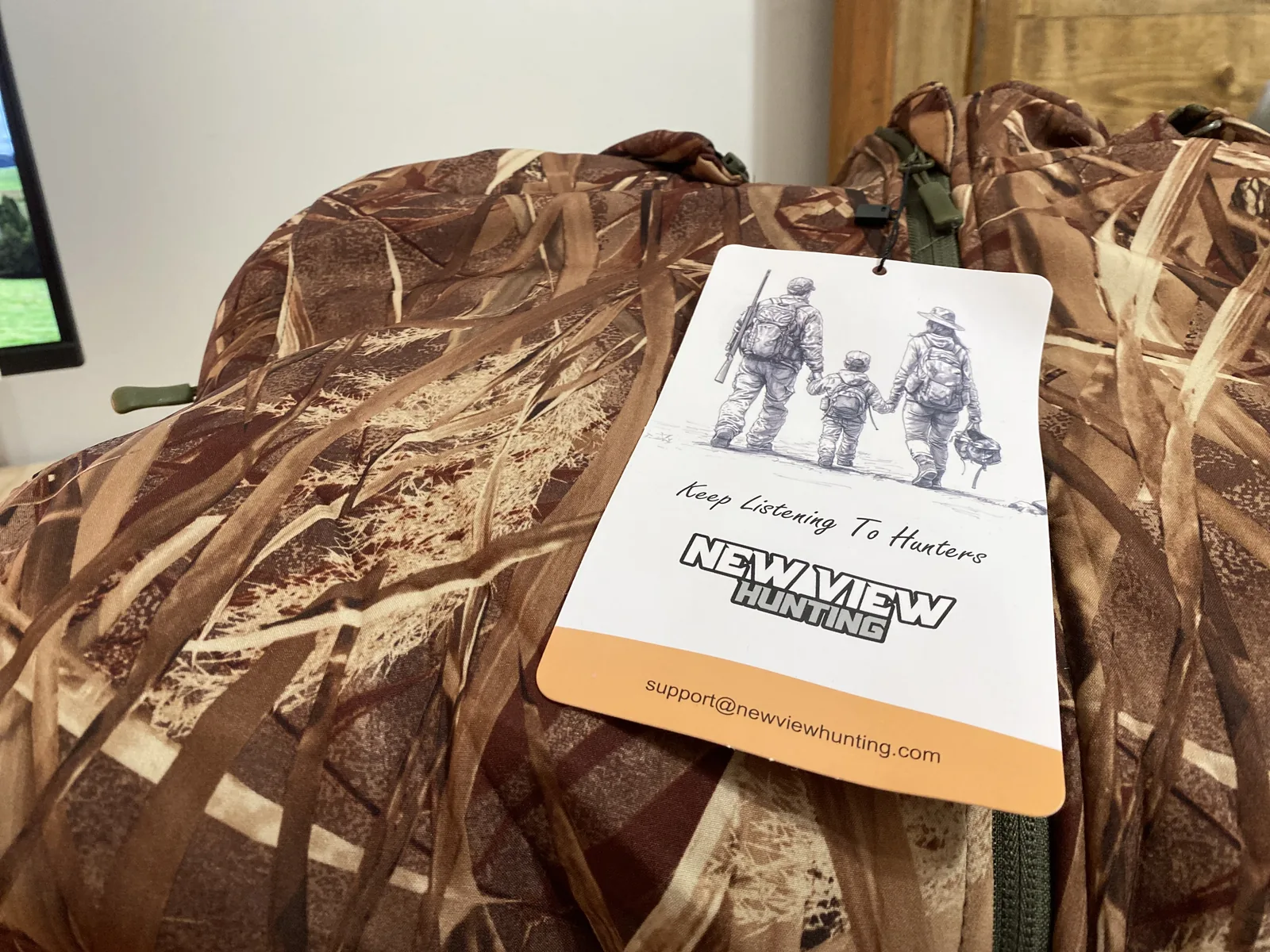 A white hang tag showing a line drawing of two adults and a child walking with hunting gear, over the words Keep Listening To Hunters and the New View Hunting logo