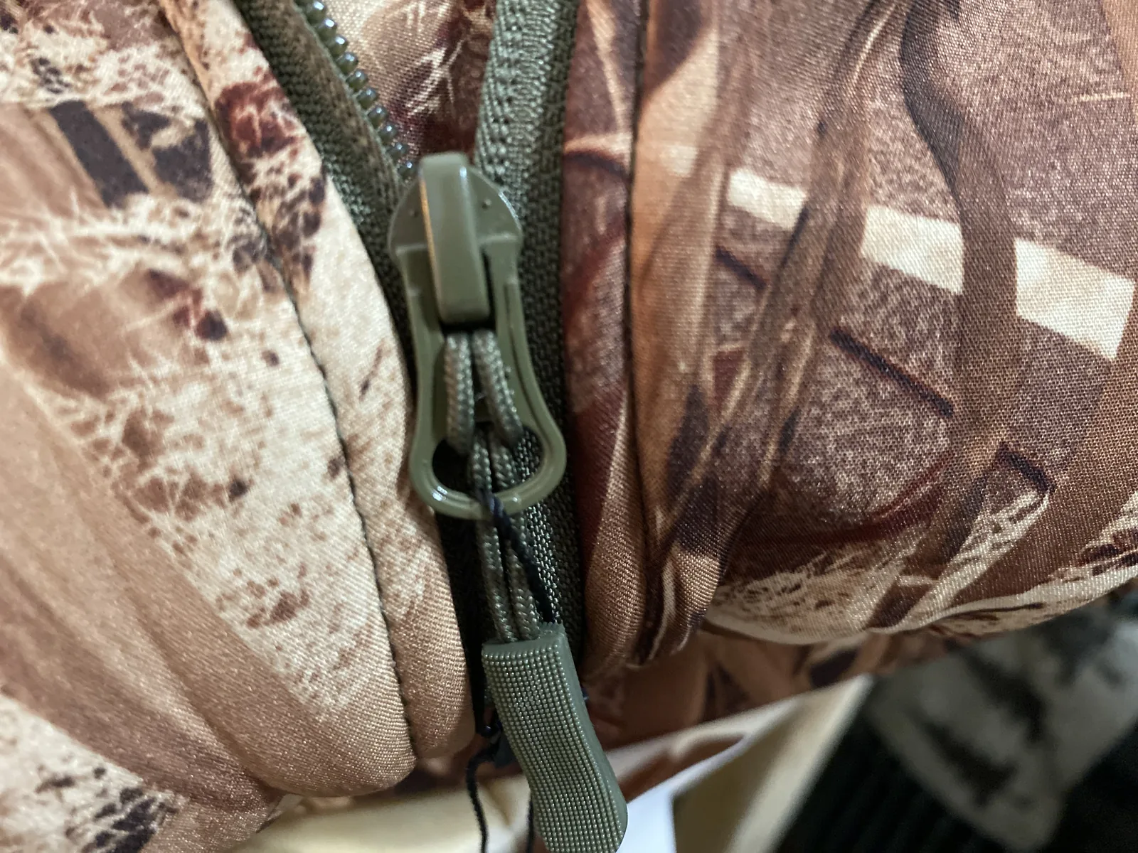 Close-up of the olive zip slider on the camo jacket with a cord pull attached