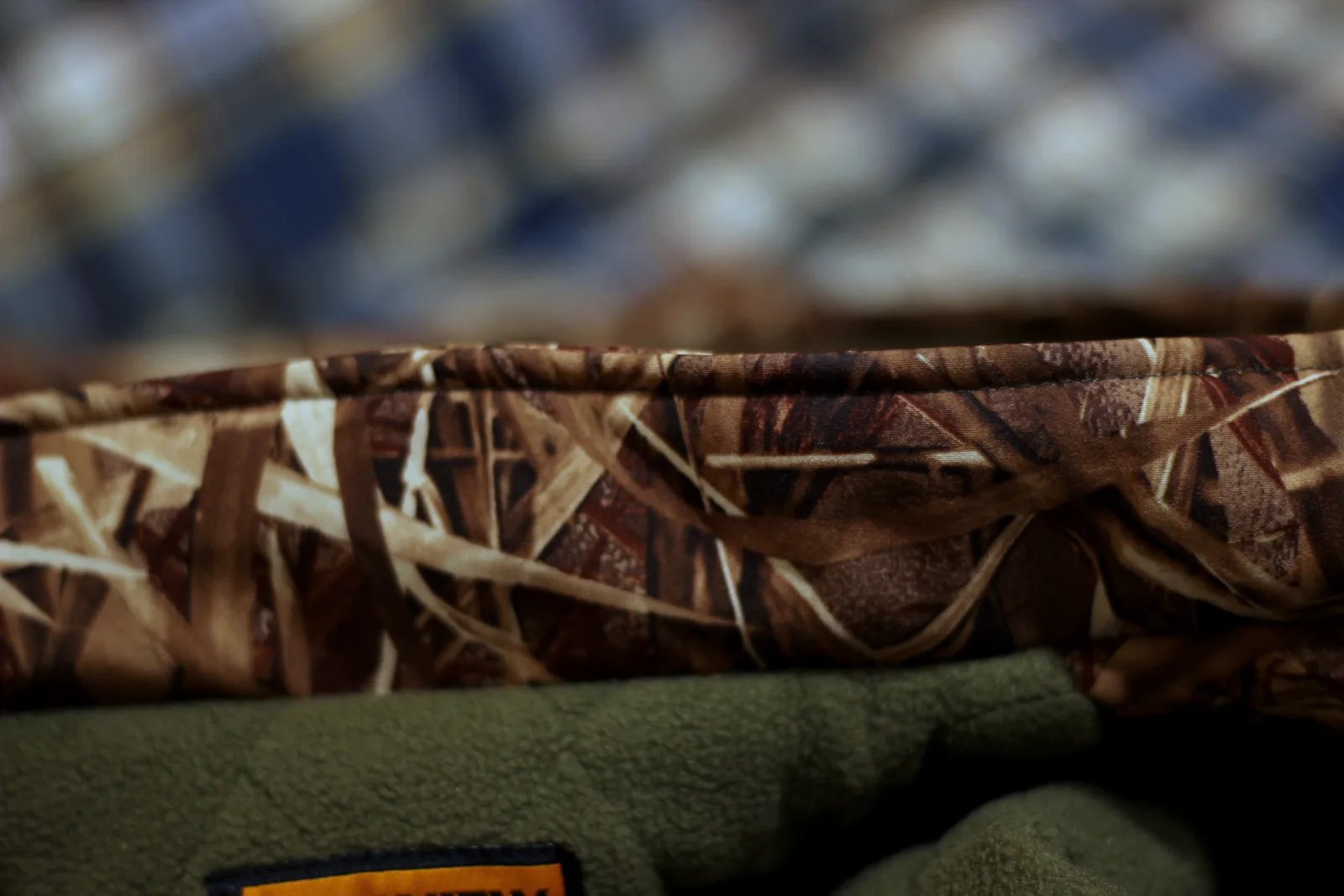 The jacket hem showing camo shell folded over the olive fleece lining with bound stitching