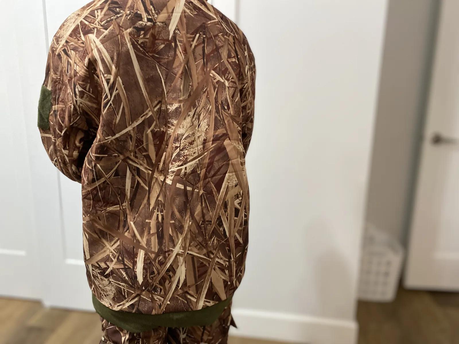 The camo hunting jacket worn, photographed from behind indoors, showing the hood down and the full back panel