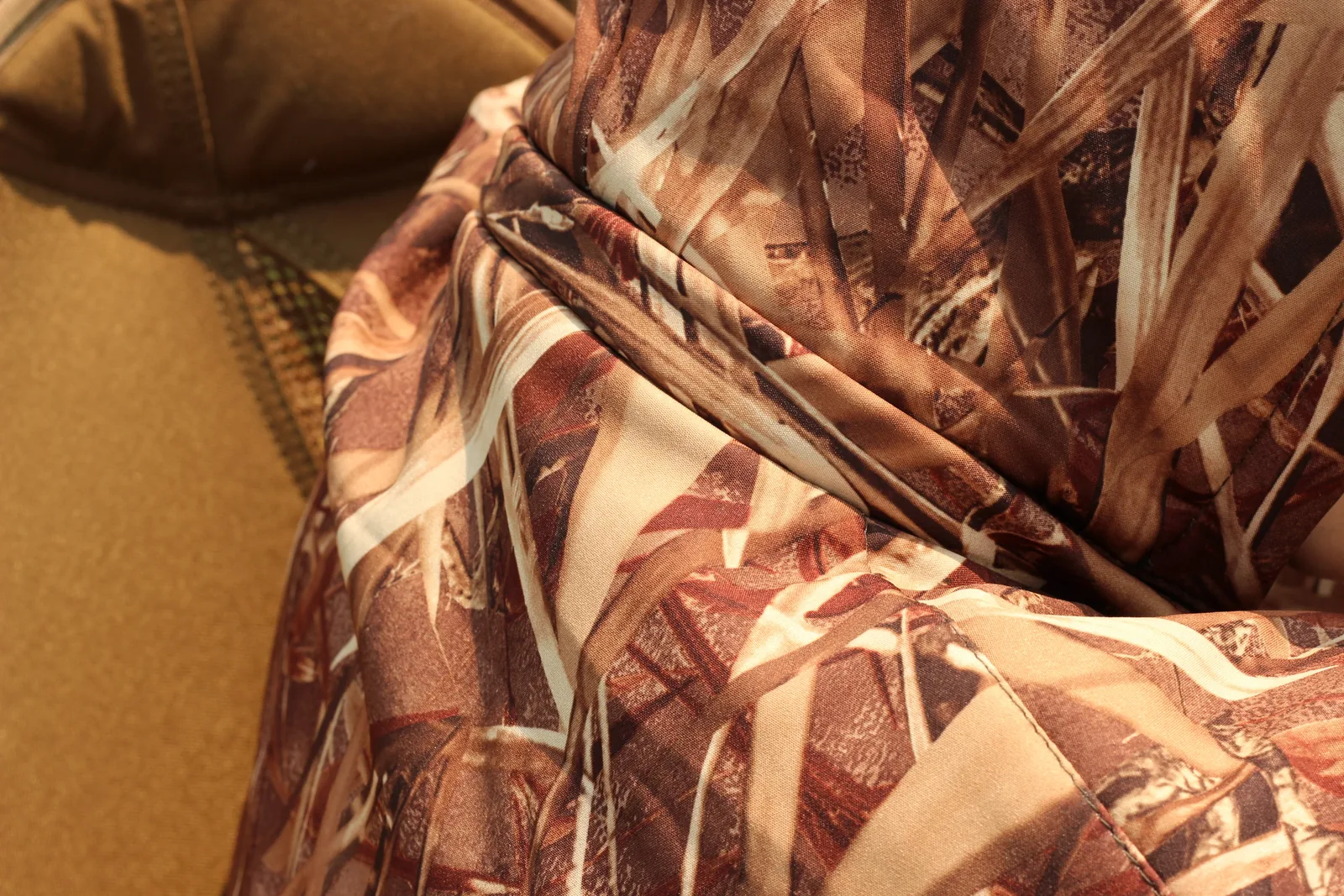 The camo jacket sleeve resting against the flat coyote-brown fabric of the camp chair