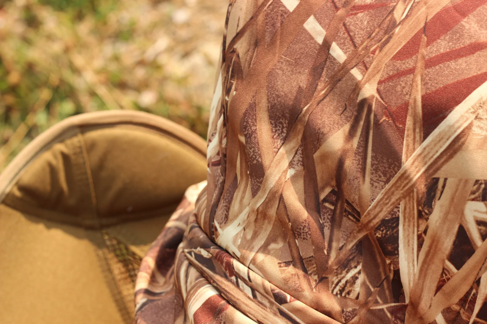 The hood and shoulder of the camo jacket against the plain seat back of the camp chair