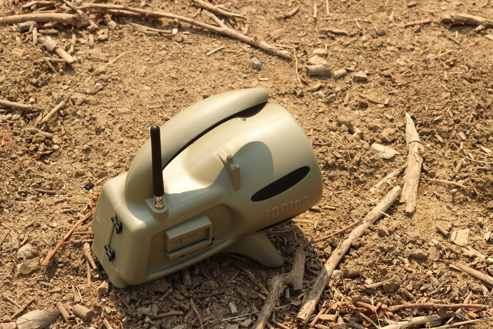 A tan electronic predator caller sitting on bare dirt and sticks a short distance from the stand