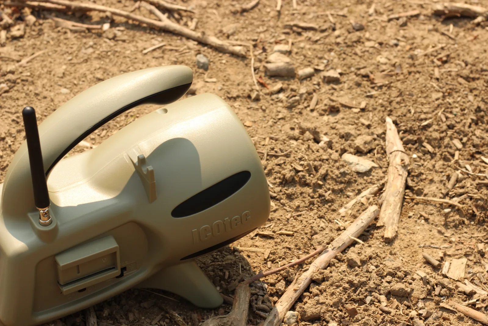 Close view of the tan electronic caller with its aerial up, resting on dry dirt and twigs
