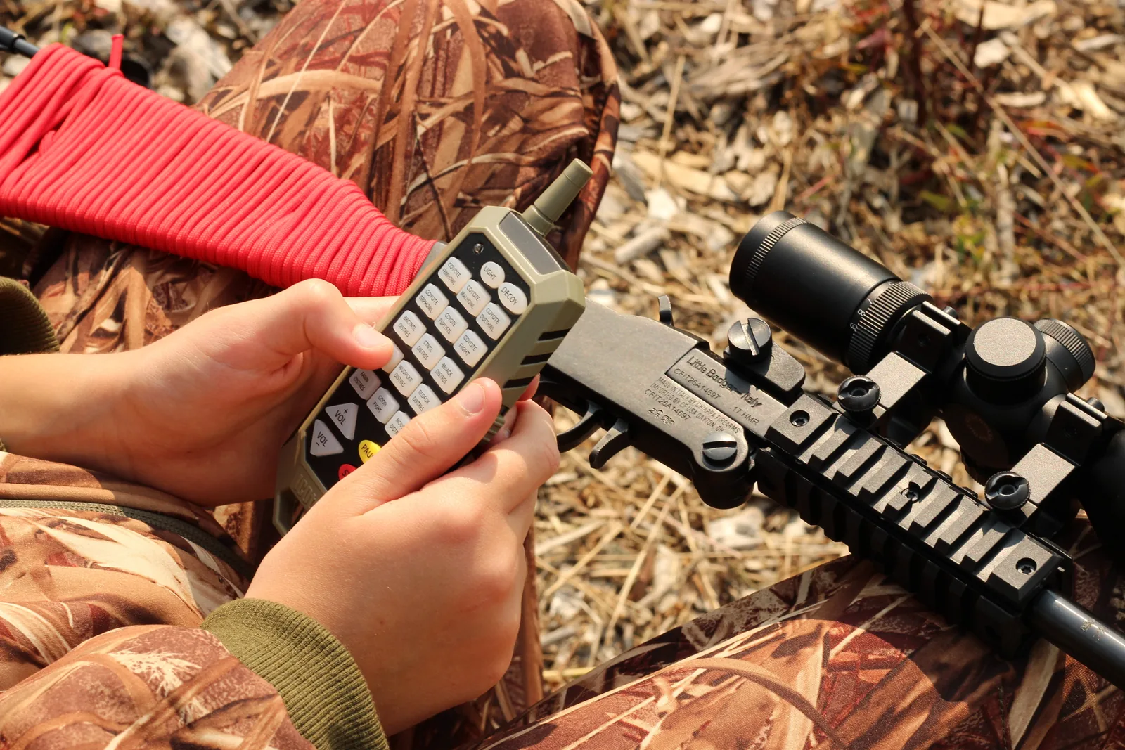 The caller remote in one hand and the scoped rifle held in the other