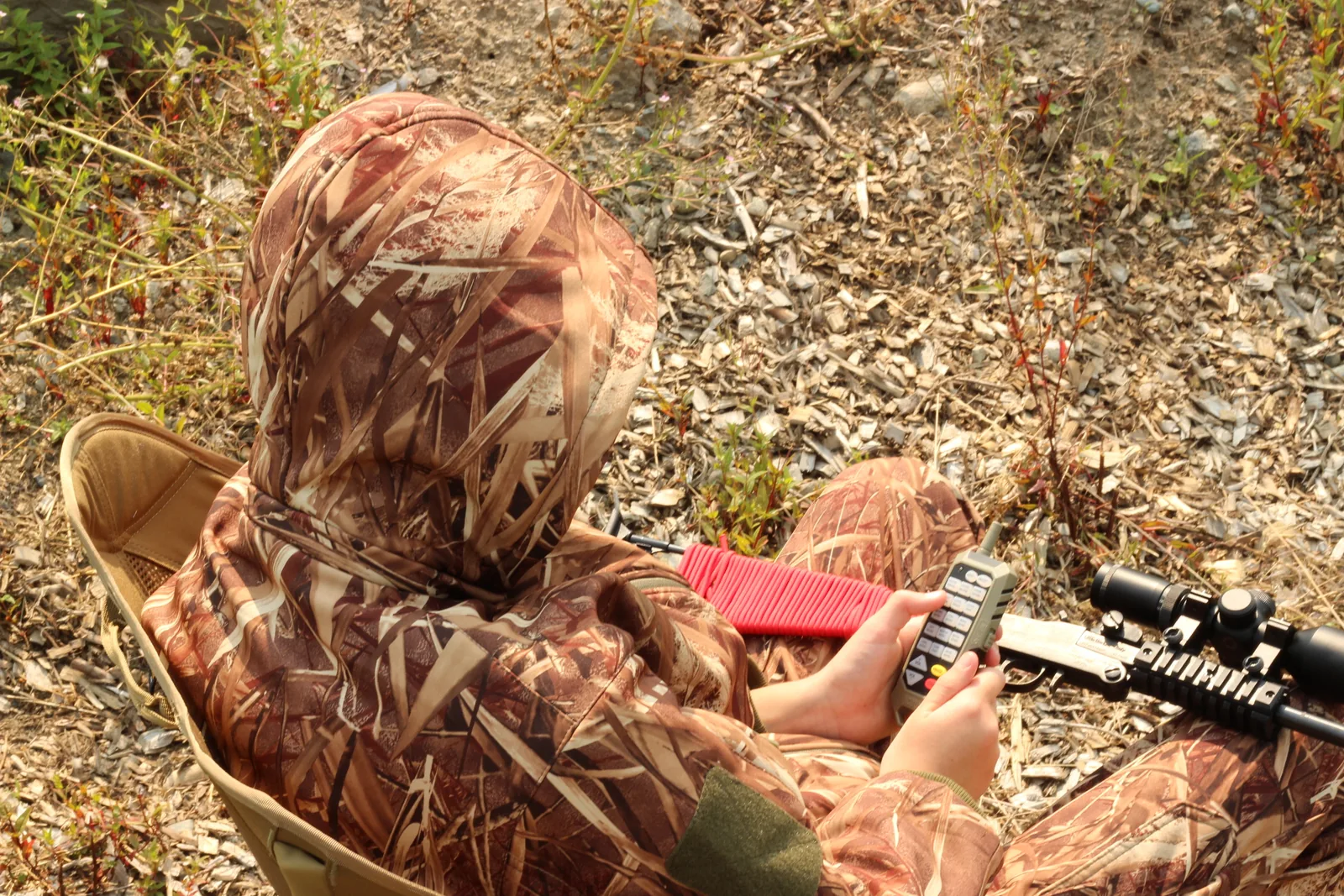 Over-the-shoulder view of the seated young hunter operating the caller with the rifle across their lap