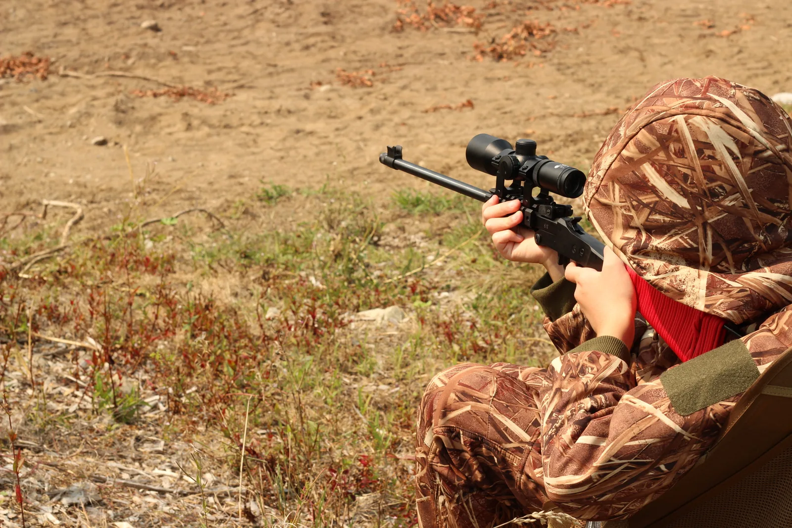 Side-on view of the seated young hunter with the rifle shouldered and the hood up