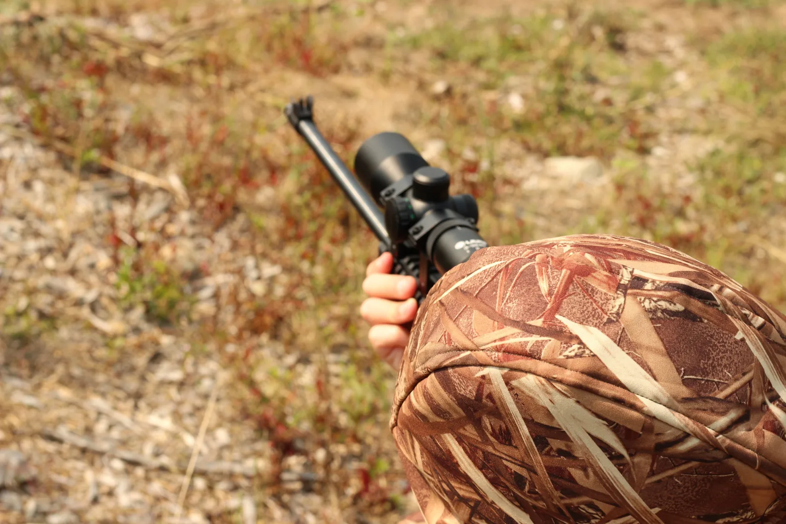 View over the hood of the seated young hunter as the scoped rifle is brought to bear