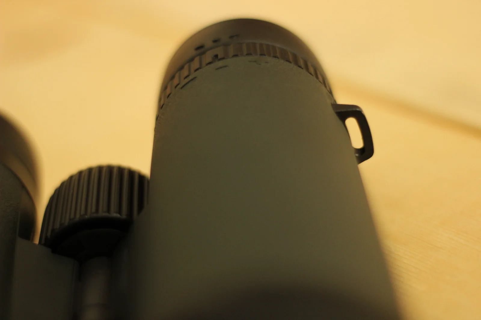 Top-down view of the two objective lens caps of the Riton 5 Primal 10x42 ED in the closed position, photographed at an angle showing both caps with the tether tabs visible on top of each cap, the rubber-armored barrel housings visible around the cap rims, with a hand barely visible at the right edge of the frame