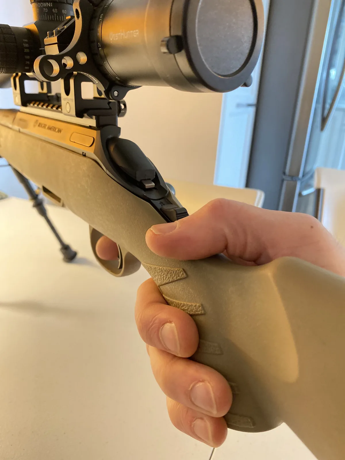 Hand wrapped around the textured FDE pistol grip of the Ruger American Ranch, finger indexed along the stock