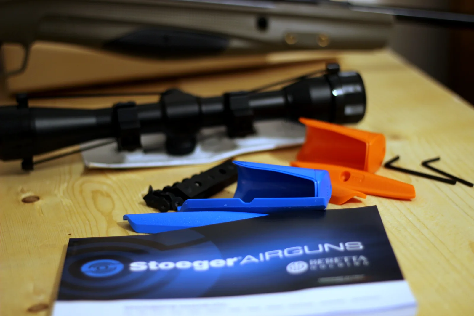 The scope, rings, hex keys, manual and coloured polymer inserts laid out on a wooden bench