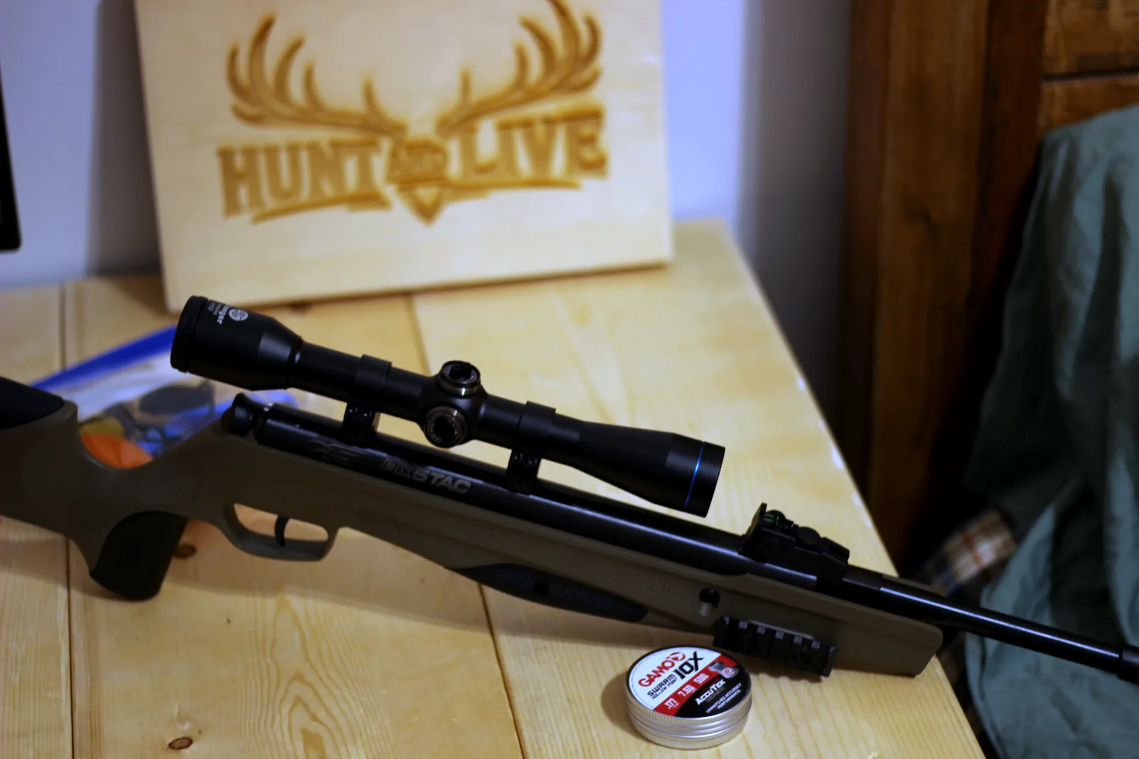 The assembled scoped rifle lying on a wooden bench in front of a Hunt and Live branded board