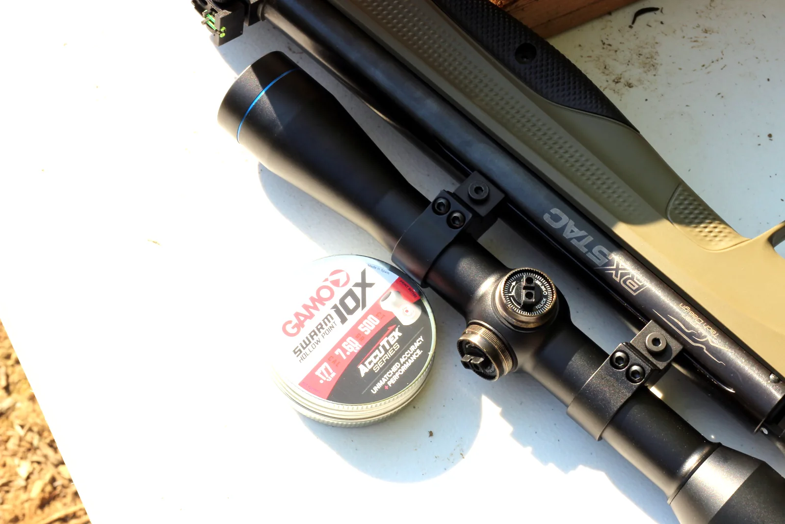 The rifle and scope beside a tin of Gamo 10X pellets on a white bench