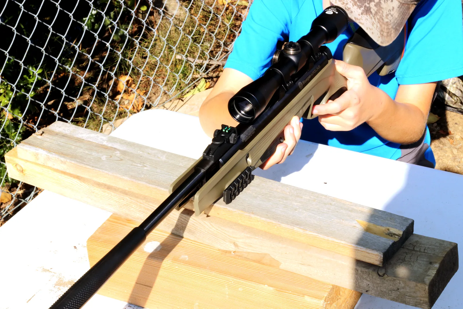 The young shooter settling behind the scope with the rifle on a wooden rest