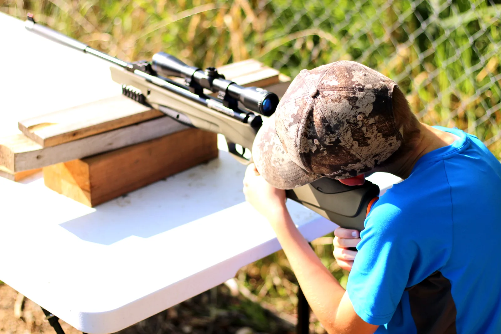 Wide view of the young shooter working the rifle from a folding bench outdoors