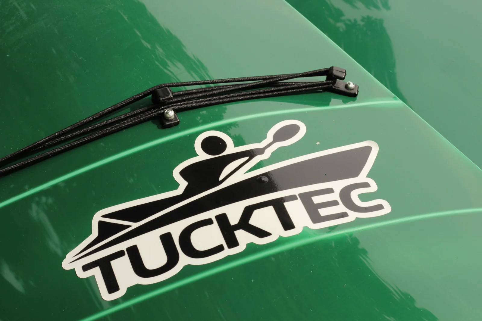 Close-up of the white-and-black TUCKTEC logo decal on the green hull with bungee deck rigging mounted above it