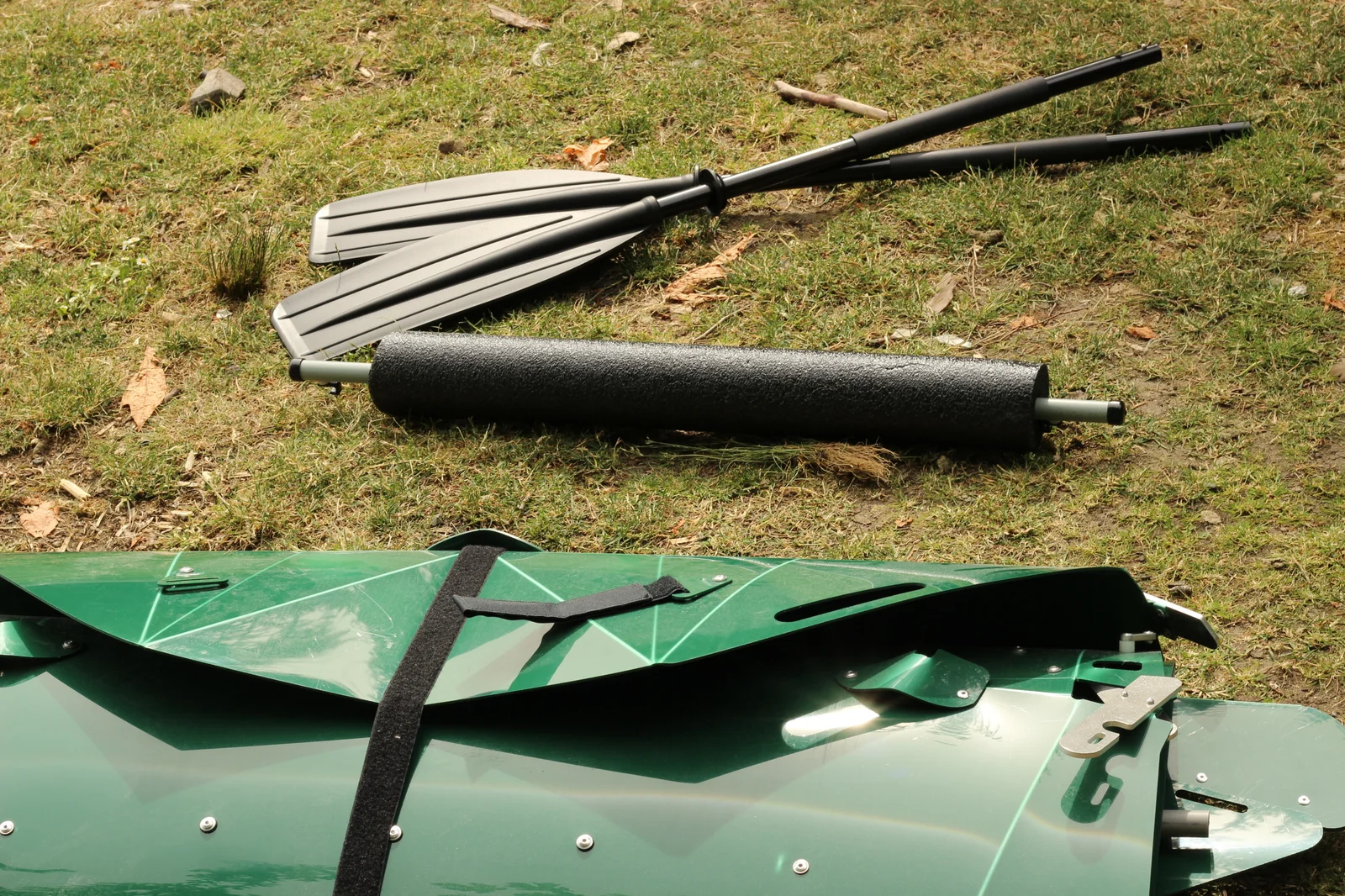 Folded Tucktec hull on grass next to the separately-purchased 2-part paddle and the snap-on foam stabilizer pontoon