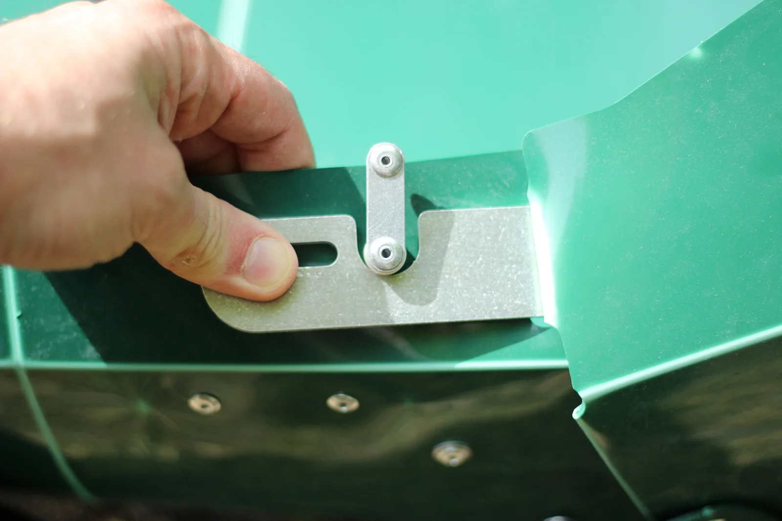 Hand holding one of the aluminum locking levers showing the slot detail with the green Tucktec hull in the background