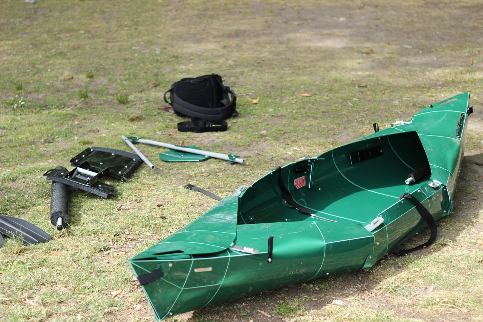 The Tucktec Pro kayak nearly fully assembled on grass with the foam stabilizer, paddle pieces, and a black seat cushion staged beside it for installation