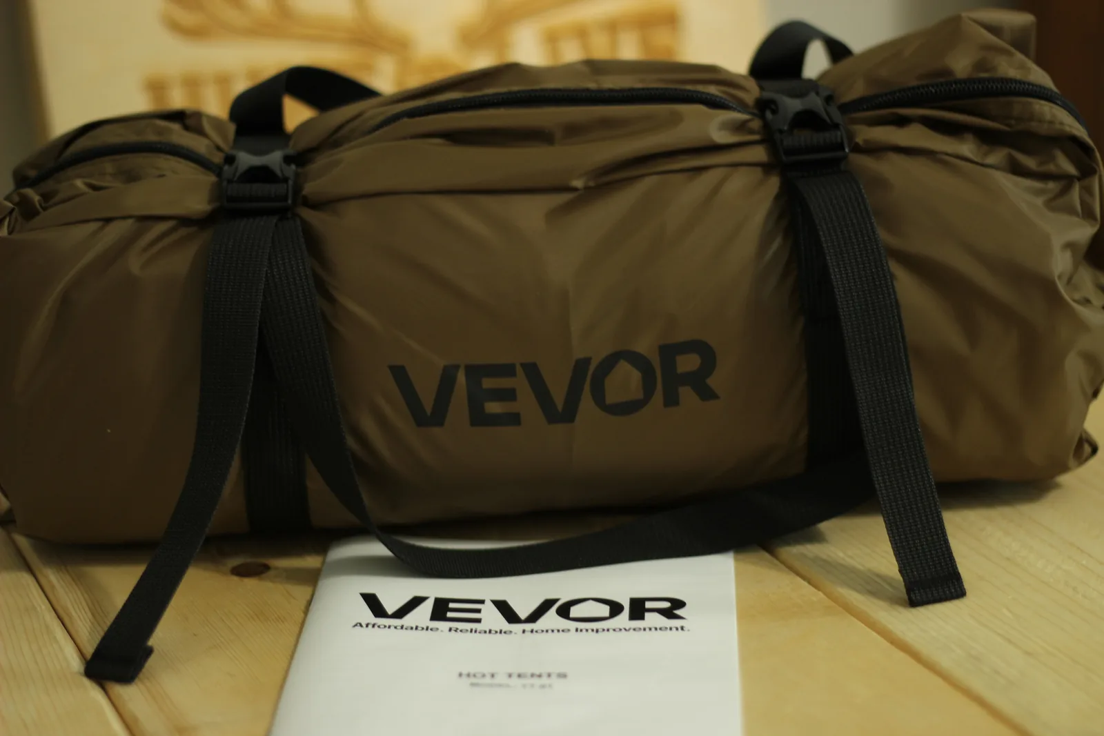 The coyote-brown packed tent in its own stuff bag with black compression straps, the folded VEVOR HOT TENTS manual lying in front of it