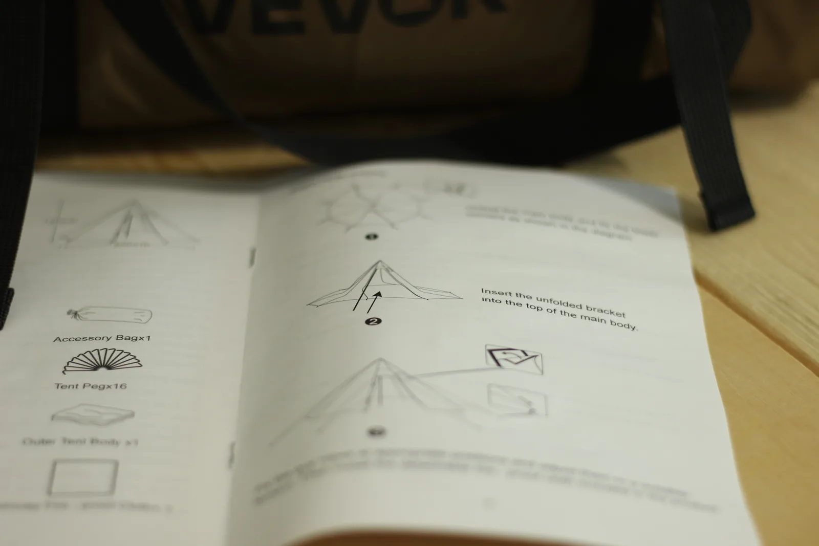 The opened manual showing a parts list with icons reading Accessory Bag x1, Tent Peg x16, Outer Tent Body x1, and a pitching diagram reading Insert the unfolded bracket into the top of the main body