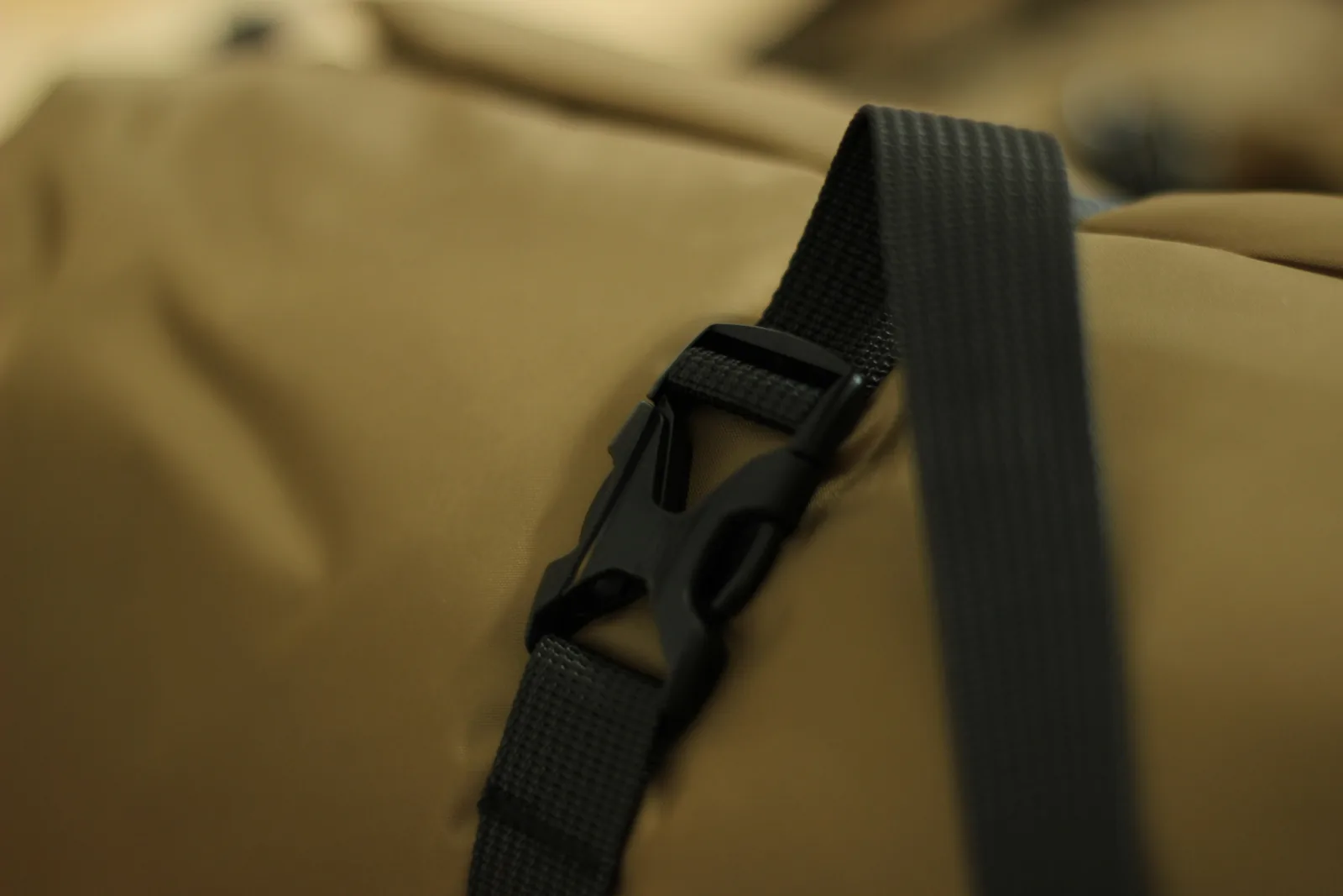 Close-up of a side-release buckle and its webbing tail against the brown bag fabric