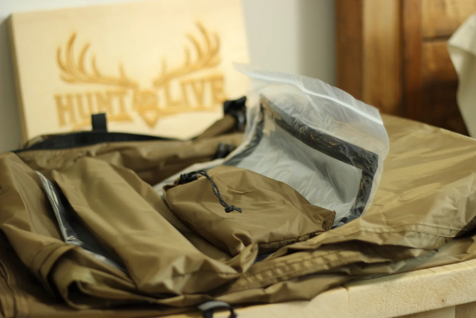 The tent contents spread on a bench: folded canopy, two drawcord pouches, and a clear packet, with the Hunt and Live plaque behind