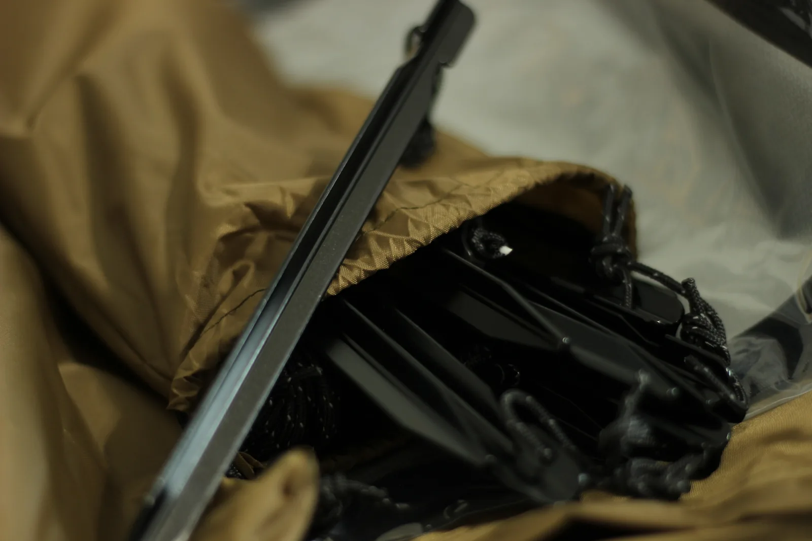 A drawcord pouch opened to show black stakes and coiled cord inside, with a pole section leaning across it