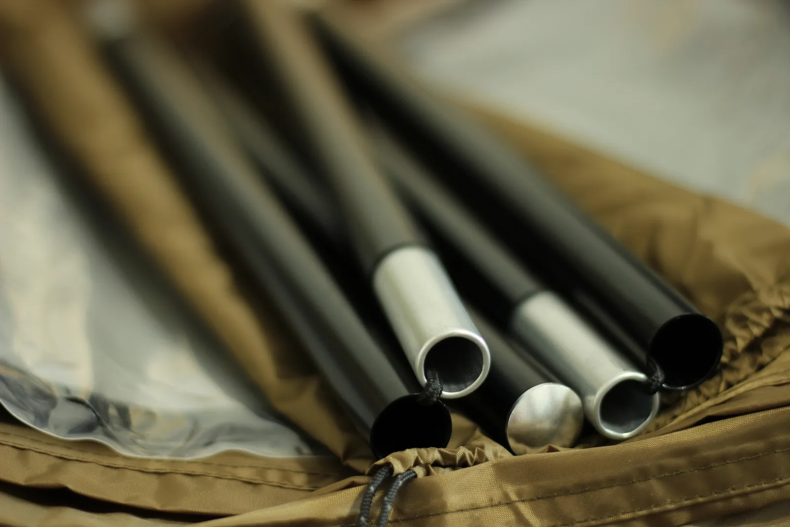 Four black anodised aluminium pole sections with silver ferrules lying on the brown tent fabric