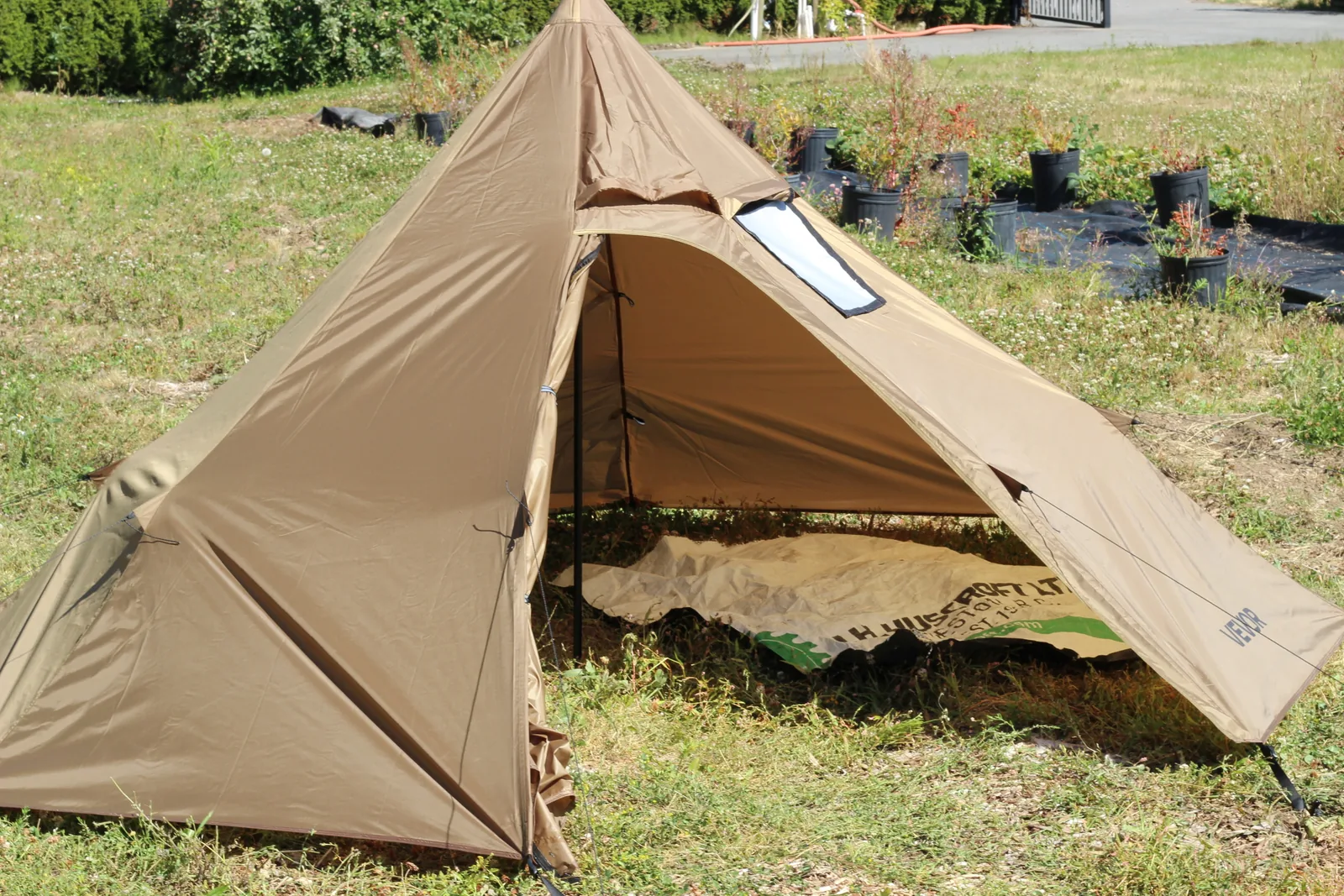 The tent pitched on grass with the door rolled open, a groundsheet visible inside, nursery pots in the background