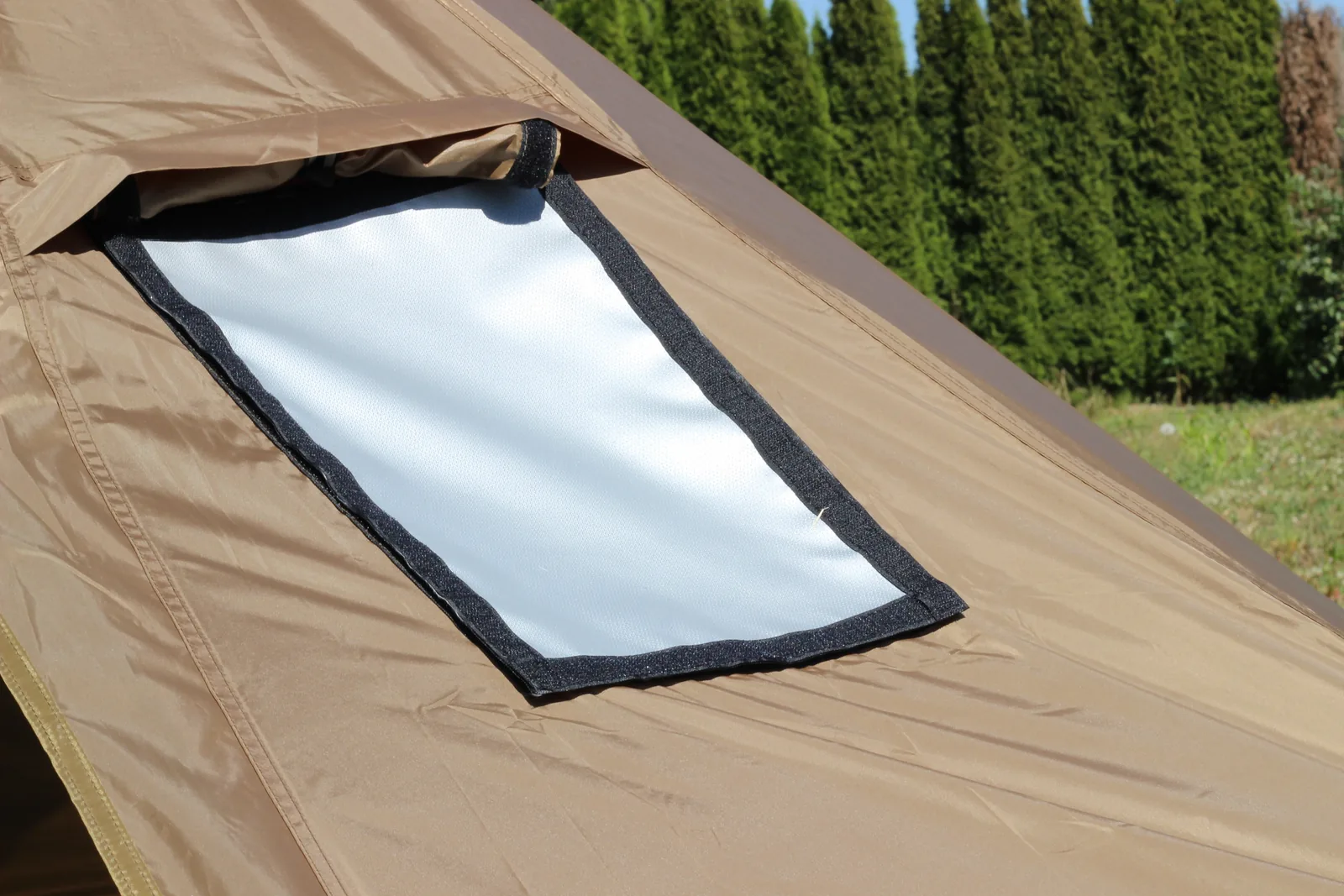 The stove jack on the pitched tent: a pale rectangular flame-retardant panel bordered in black hook-and-loop tape, set into the brown canopy