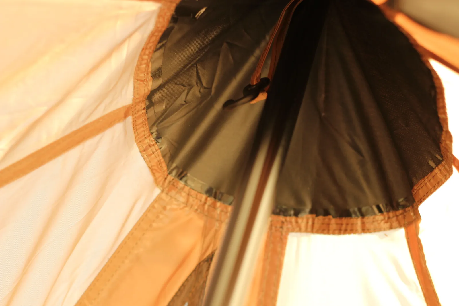 Looking up inside the tent at the dark reinforced apex cap where the panels meet and the pole tip sits