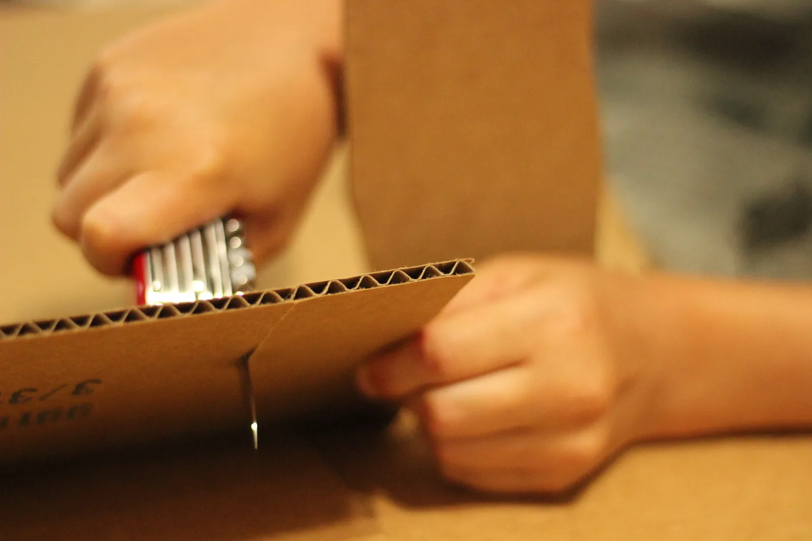 A child's hands using the red Cellidor-handled Victorinox SwissChamp large knife to cut through a corrugated cardboard panel along a clean cut line
