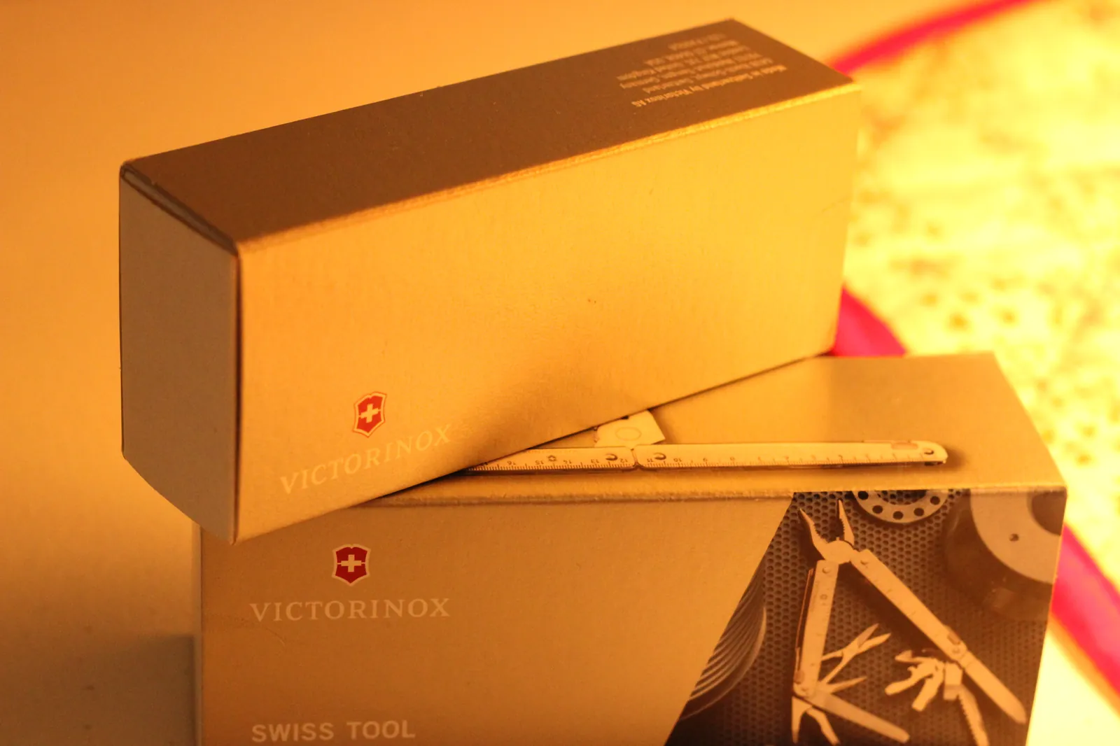 Two Victorinox boxes stacked on the Swiss Tool box with a folded ruler partially extended showing the matte tan finish and red shield