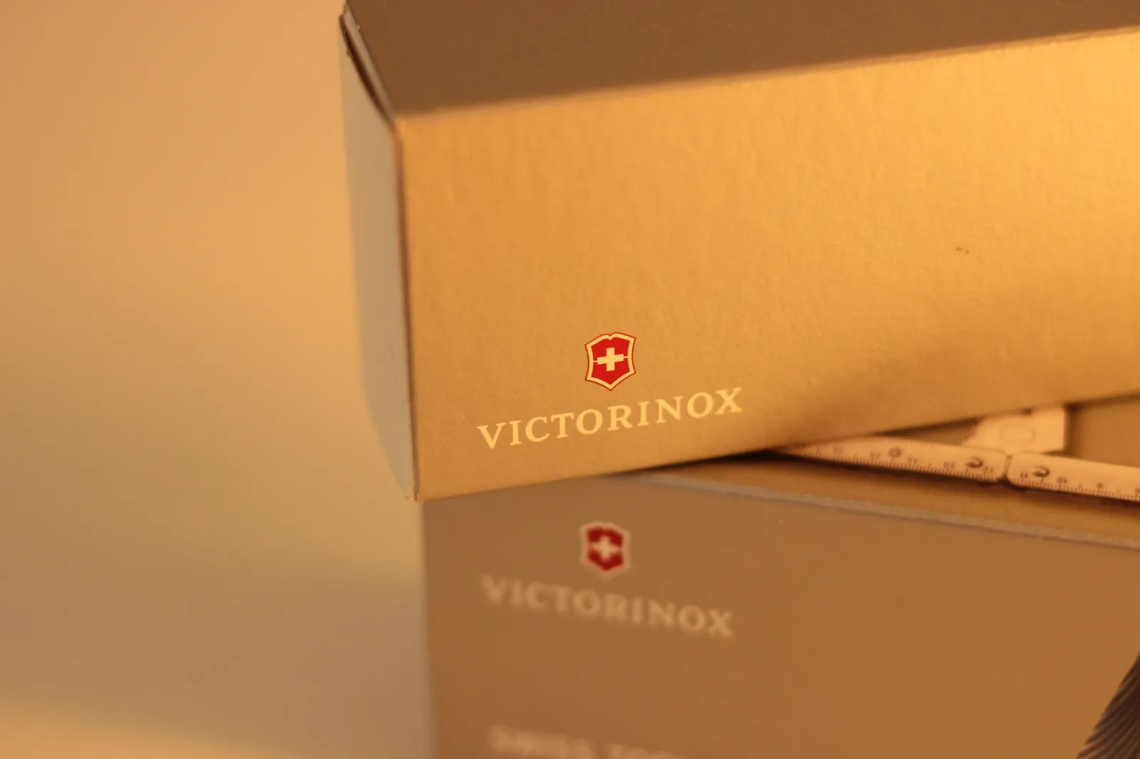 Two Victorinox boxes stacked together — the smaller SwissChamp box on top of the larger Swiss Tool MX Clip box, both in the unmistakable matte tan finish with the Victorinox shield