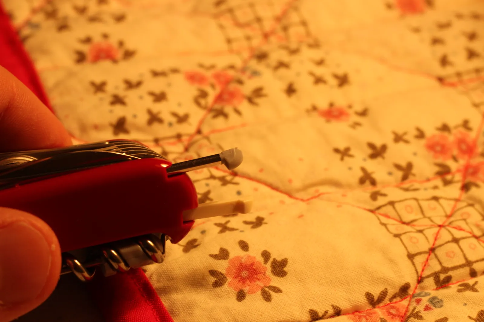 The SwissChamp's white plastic toothpick being slid back into its slot in the red Cellidor scale on a floral quilt surface