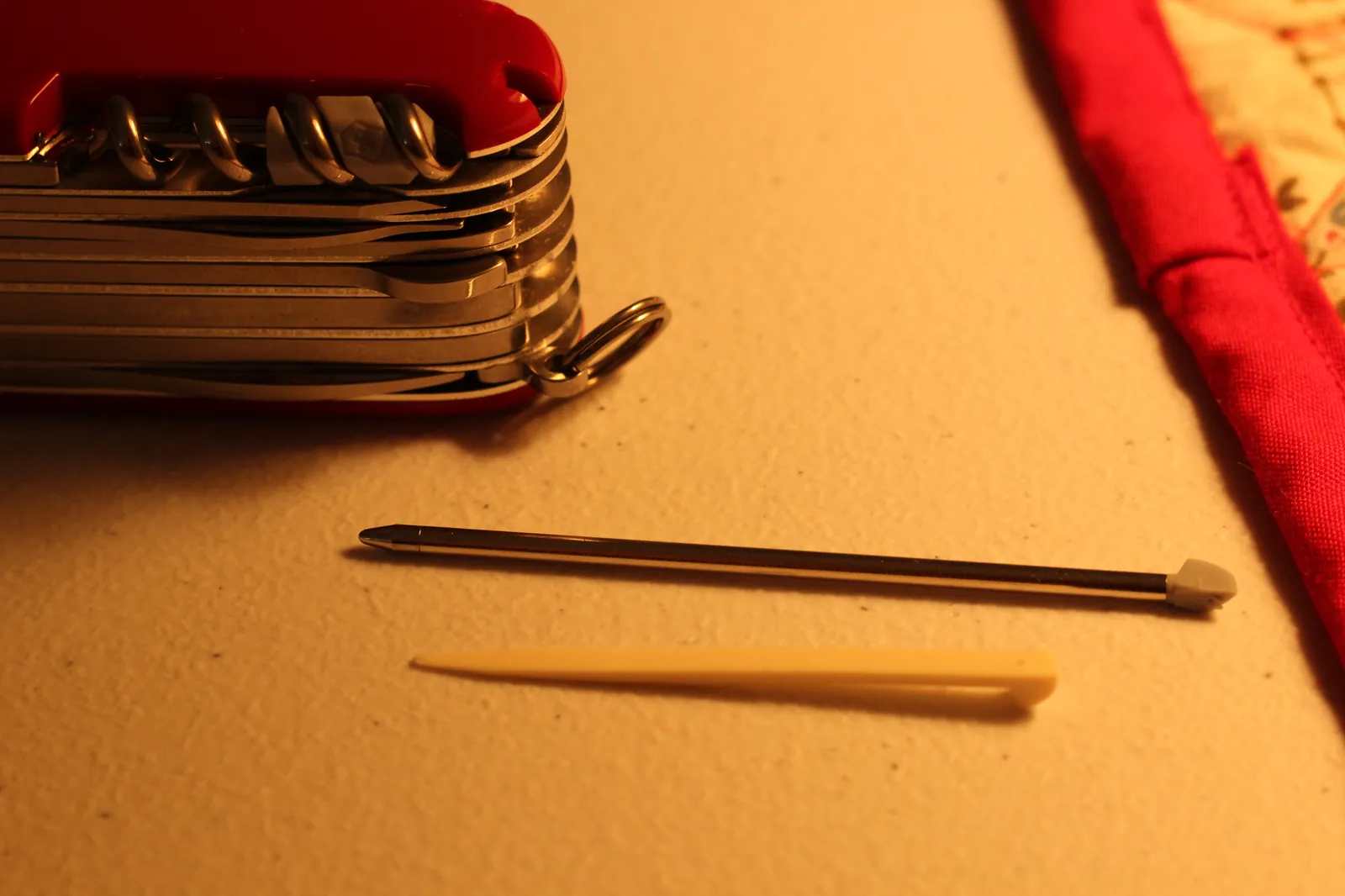 The SwissChamp's removable Phillips screwdriver and the white plastic toothpick laid out on a tan surface beside the closed knife