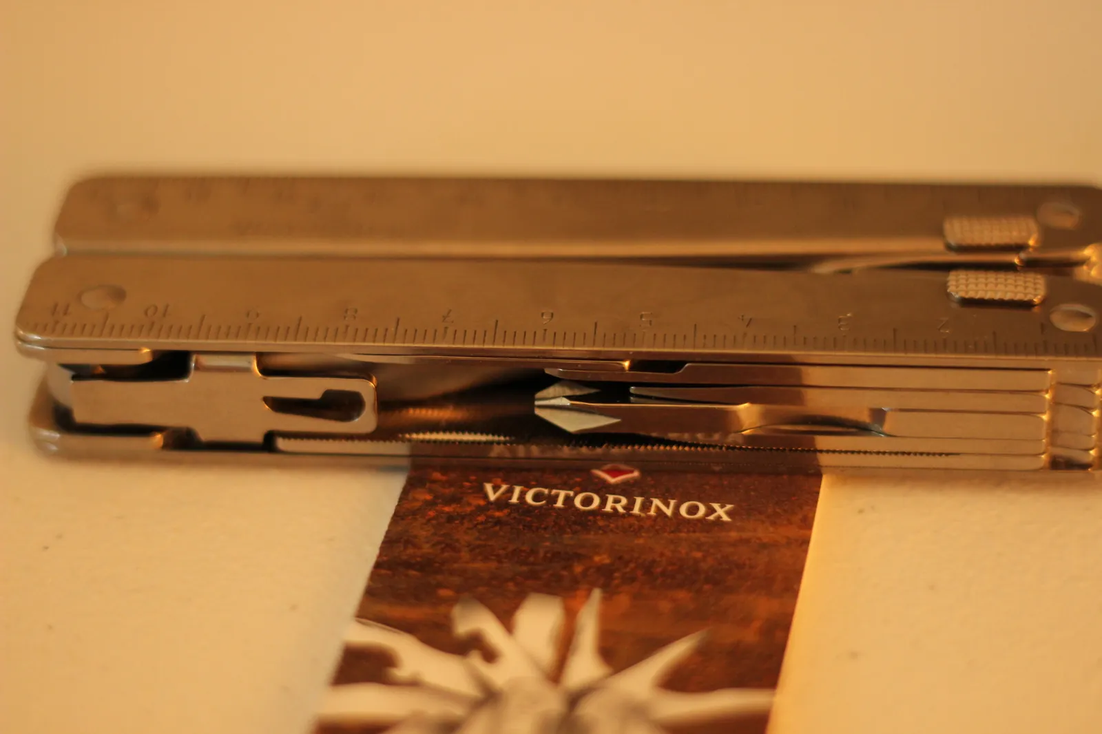 The Swiss Tool MX Clip closed flat on top of a Victorinox marketing card showing the ruler edge and the VICTORINOX wordmark on the brown landscape card underneath